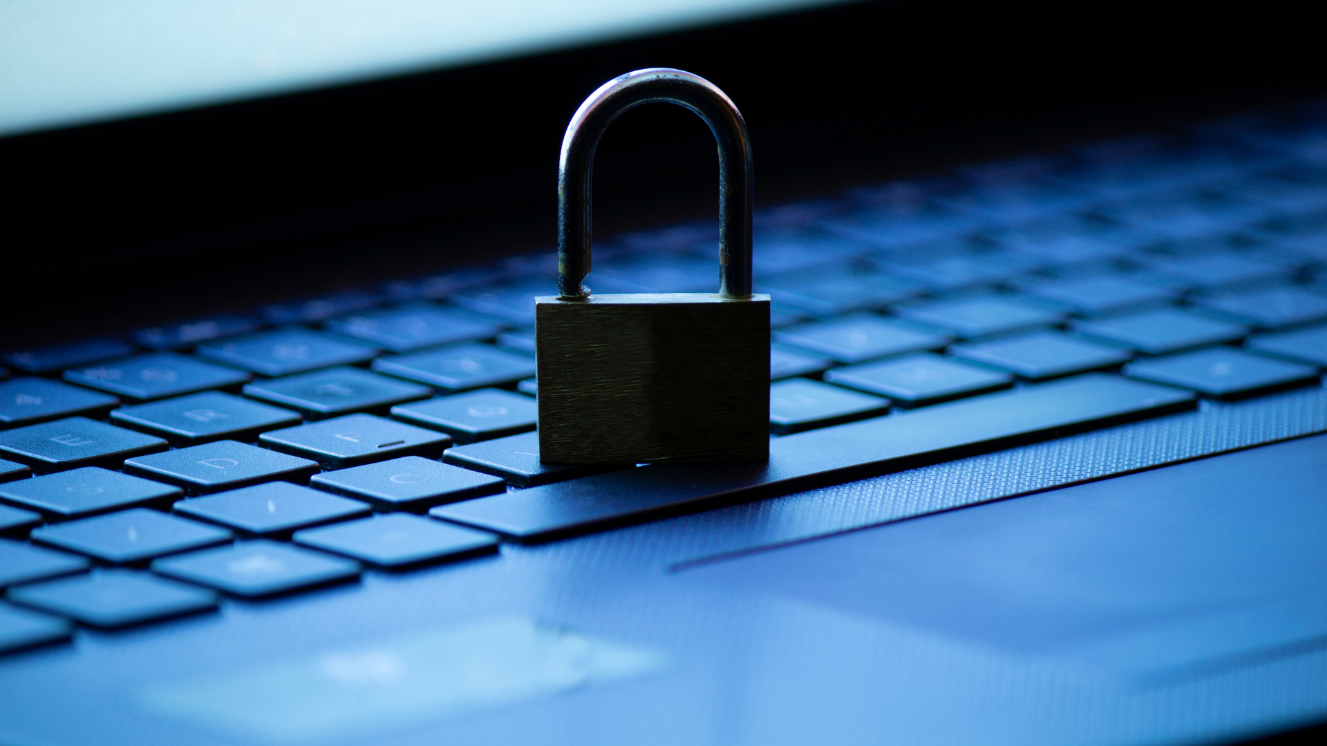 Das Bild zeigt ein offenes Vorhängeschloss auf der Tastatur eines Laptops, was symbolisch für Zugänglichkeit oder Sicherheitsrisiken in Bezug auf die auf dem Gerät gespeicherten Daten stehen kann. Die blau beleuchtete Tastatur betont den technologischen Kontext, während das offene Schloss die Bedeutung von Cybersicherheit und den Schutz digitaler Informationen hervorhebt.