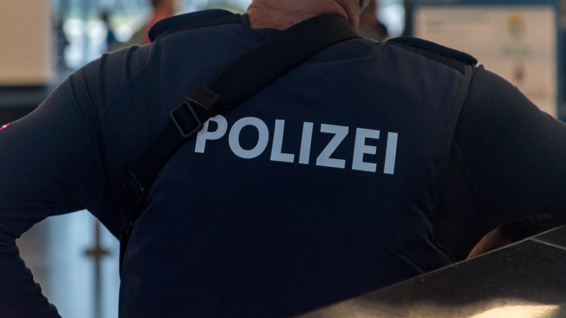 Das Bild zeigt die Rückenansicht eines Polizeibeamten, der eine dunkelblaue Uniform mit dem weißen Schriftzug