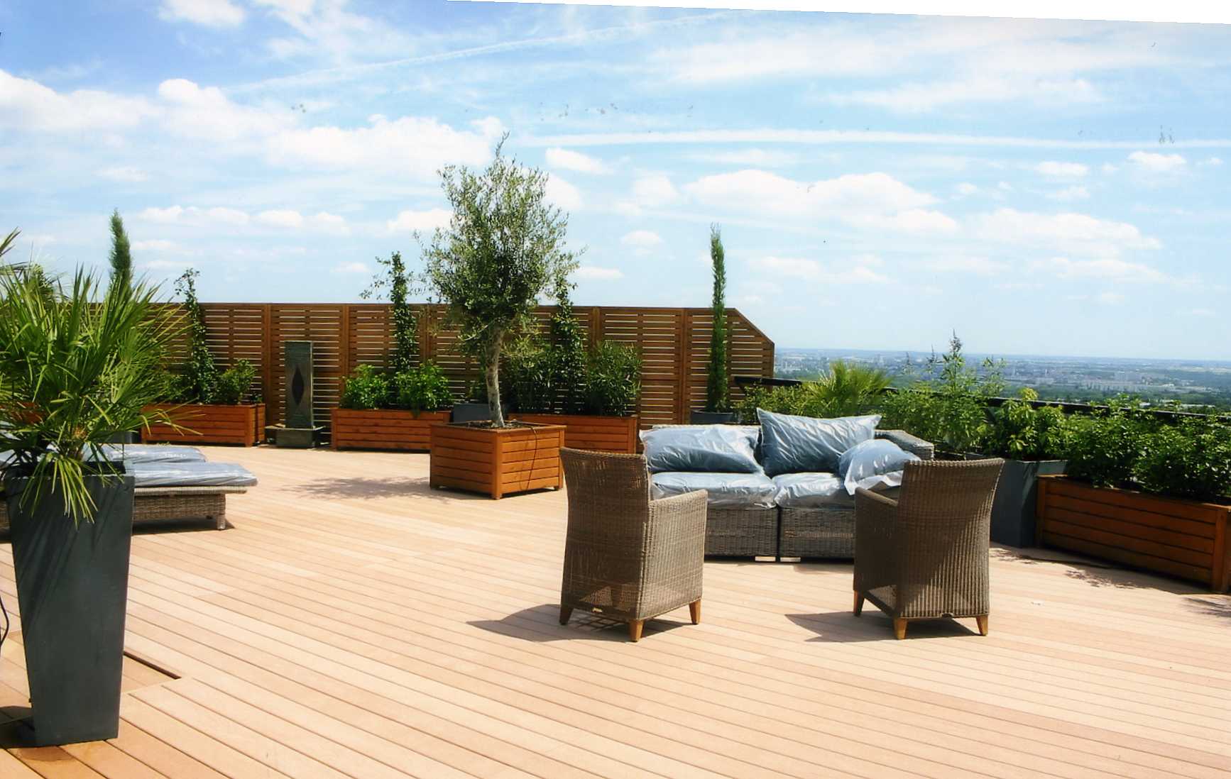 Plancher de terrasse en bois composite couleur claire, bacs en bois sur mesure, bacs et pots en fiberstone, plantes et olivier, fontaine à eau, claustras ( brise vue) en bois sur mesure.