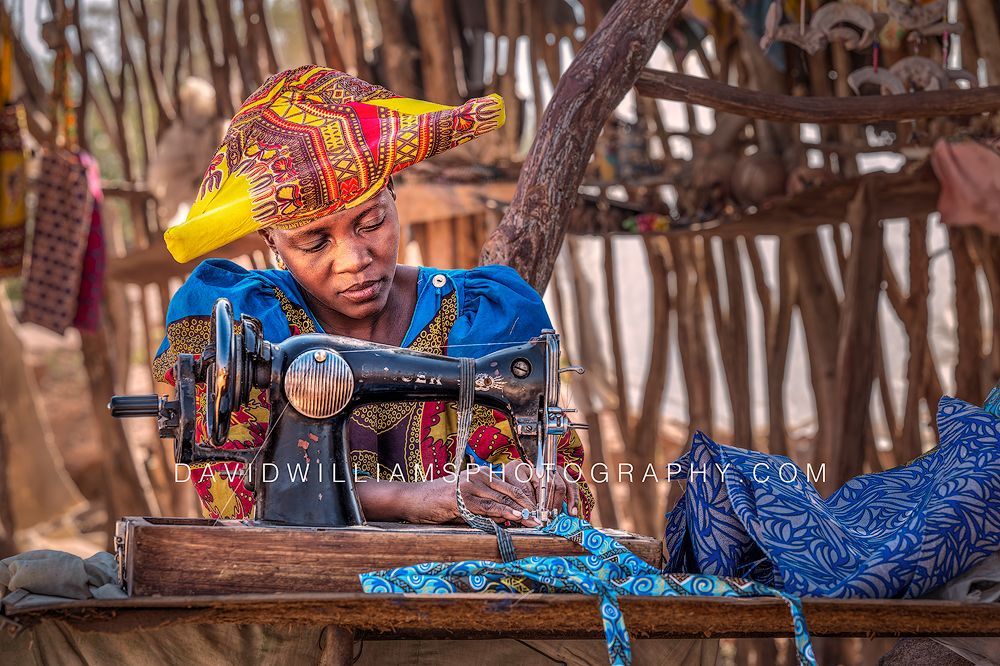 Herero woman in Victorian-style dress working at a sewing machine in her roadside craft stall near Uis, Damaraland, Namibia.