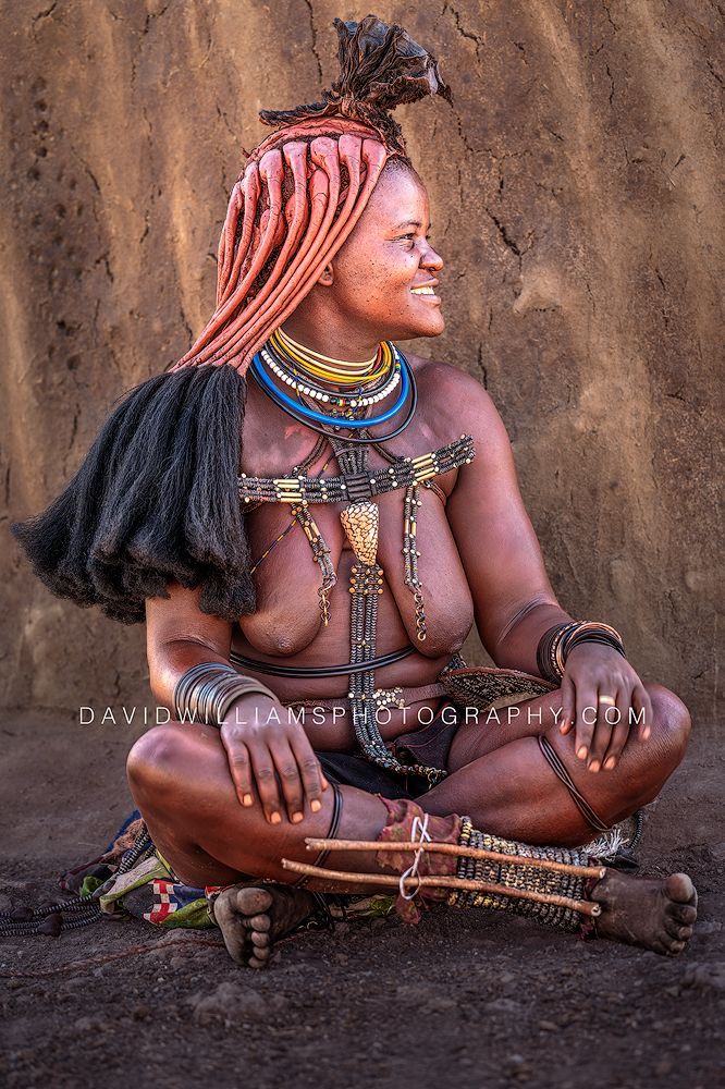Smiling Himba woman beside her mud home turning her head to show her ozondato hair in Damaraland, Namibia.