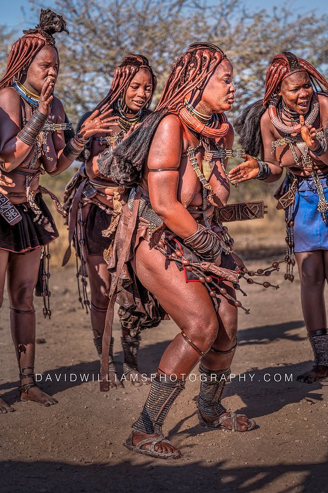 Vertical image of four Himba women performing the Ondjongo dance of happiness in traditional clothing with ozondato hair in Damaraland, Namibia.