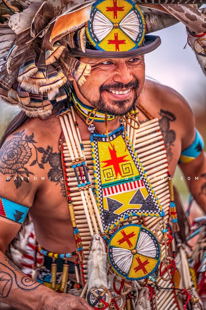 A Hopi Indian man smiling in ornate traditional clothing, photographed in a vertical fine art portrait capturing cultural storytelling and detail.