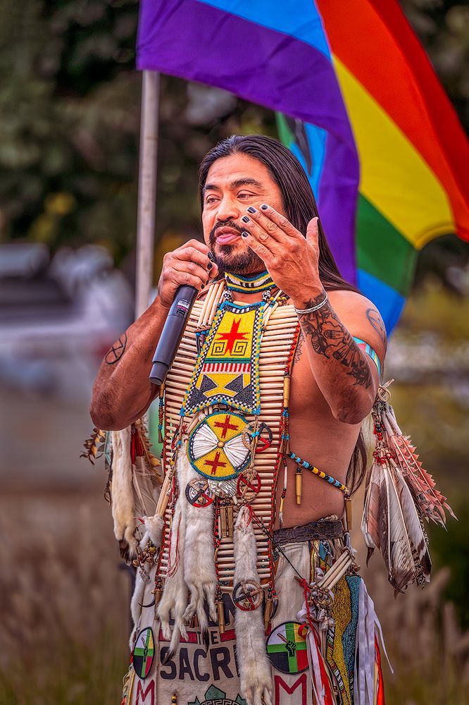 Hopi Indian man in traditional tribal clothing speaking to a crowd about his heritage and educational achievements.