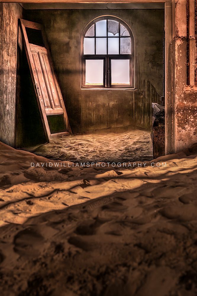 Sand-filled Kolmanskop room with an arched window, representing the African Landscape Fine Art Photography gallery by David Williams.