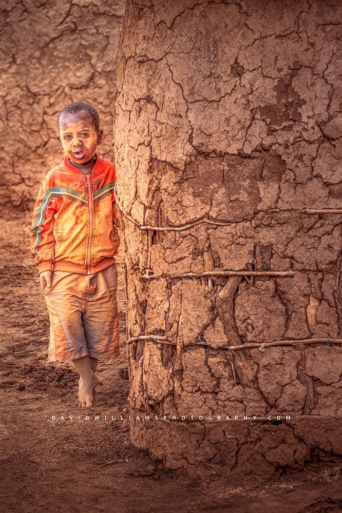A young Maasai boy standing next to his mud home, Kenya Africa