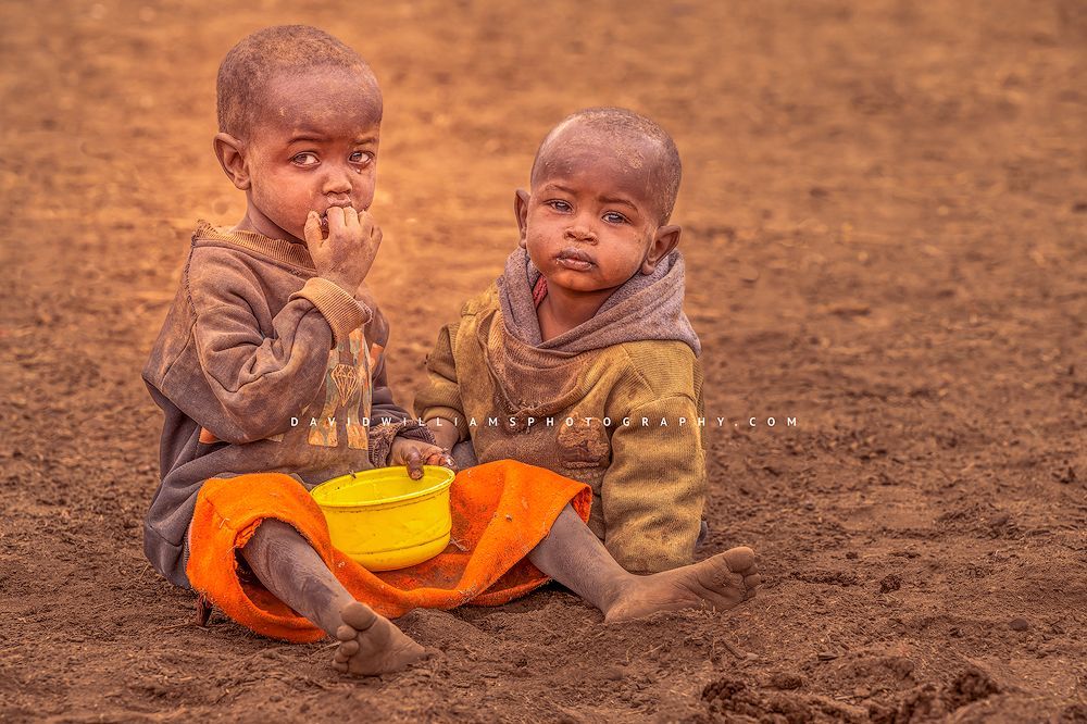 2 Maasai boys in worn out clothing eating a meal, Kenya, Africa