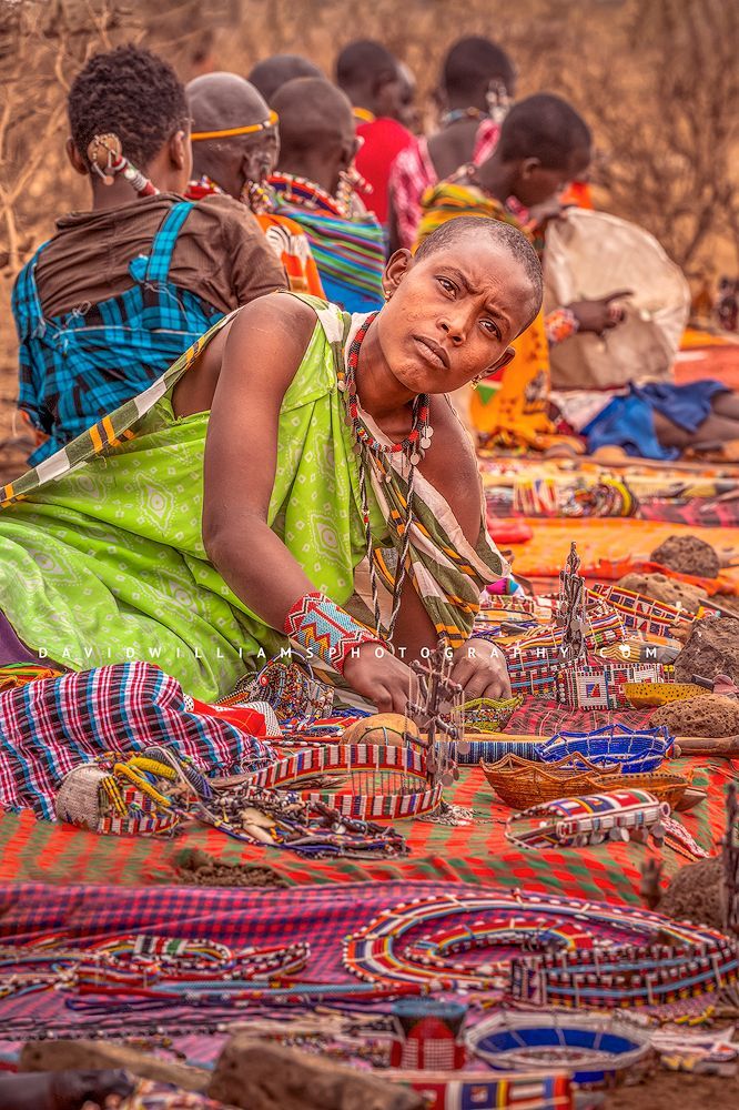 A Maasai Women on colorful rug showing off the hand made jewelry for sale, Kenya, Africa