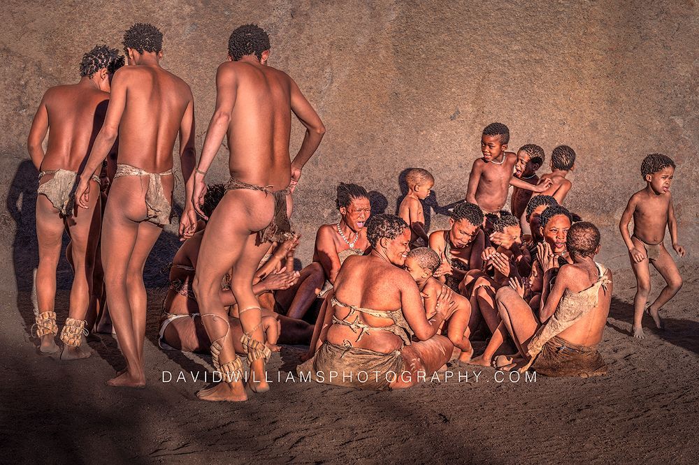 San men and youth perform a traditional dance around women caring for toddlers near Spitzkoppe, Namibia.
