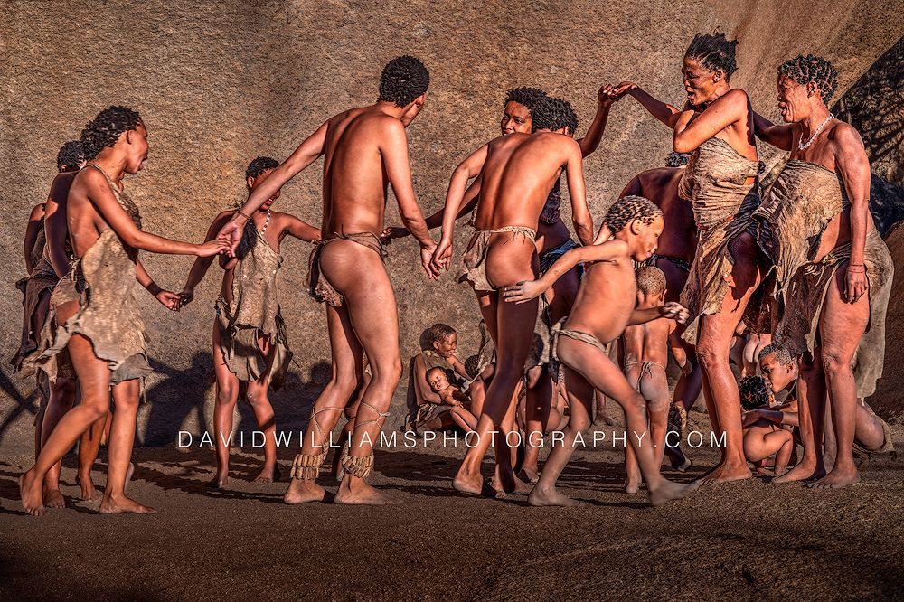 San Tribe men, women, and children perform a traditional dance in late-day sun near Spitzkoppe, Namibia.