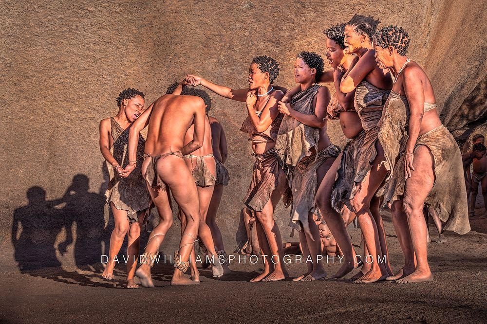 San Tribe adults sing and dance while performing a traditional ritual dance in late-day sun near Spitzkoppe, Namibia.