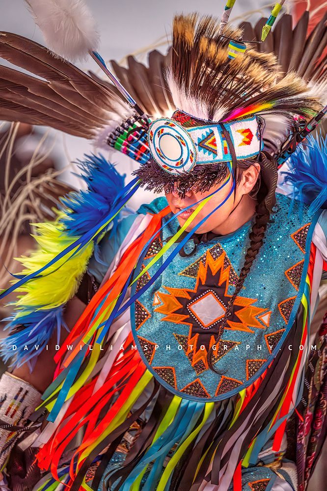 Close-up vertical portrait of a Navajo Indian performing a War Dance in full regalia, showing a colorful feathered headdress and ornate storytelling details.