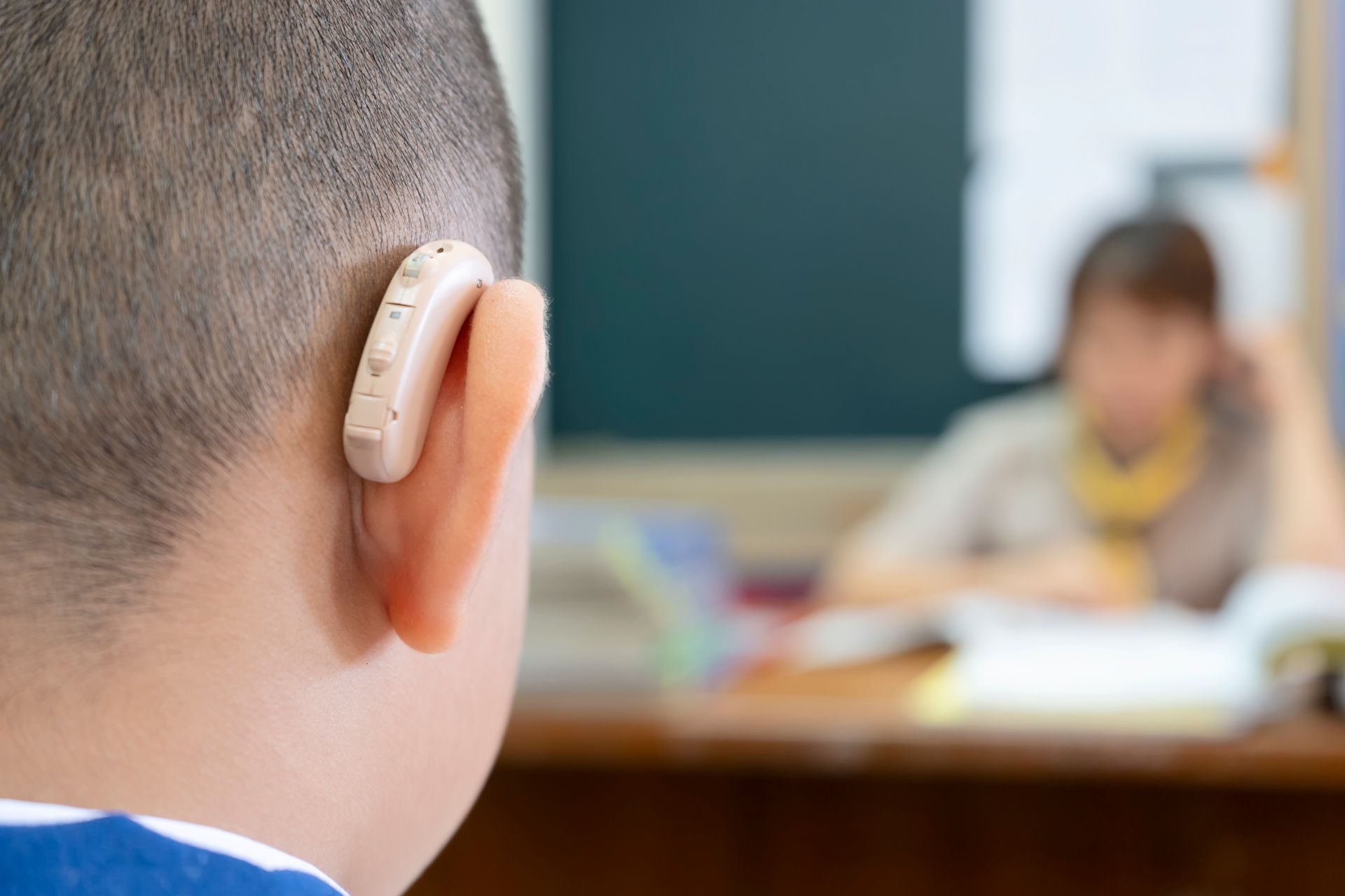 Niño con discapacidad auditiva visto desde atrás con un audífono en una de sus orejas