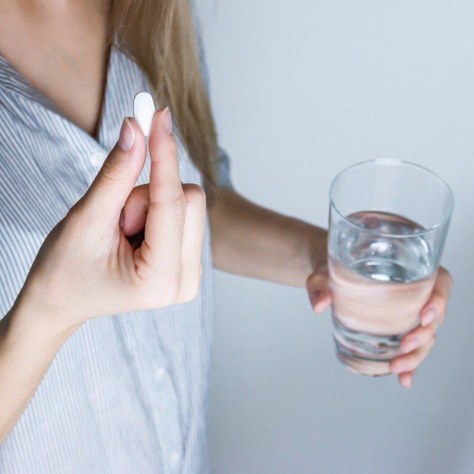 Woman holding a pill and glass of water, illustrating stress symptom support through Steady Sense.