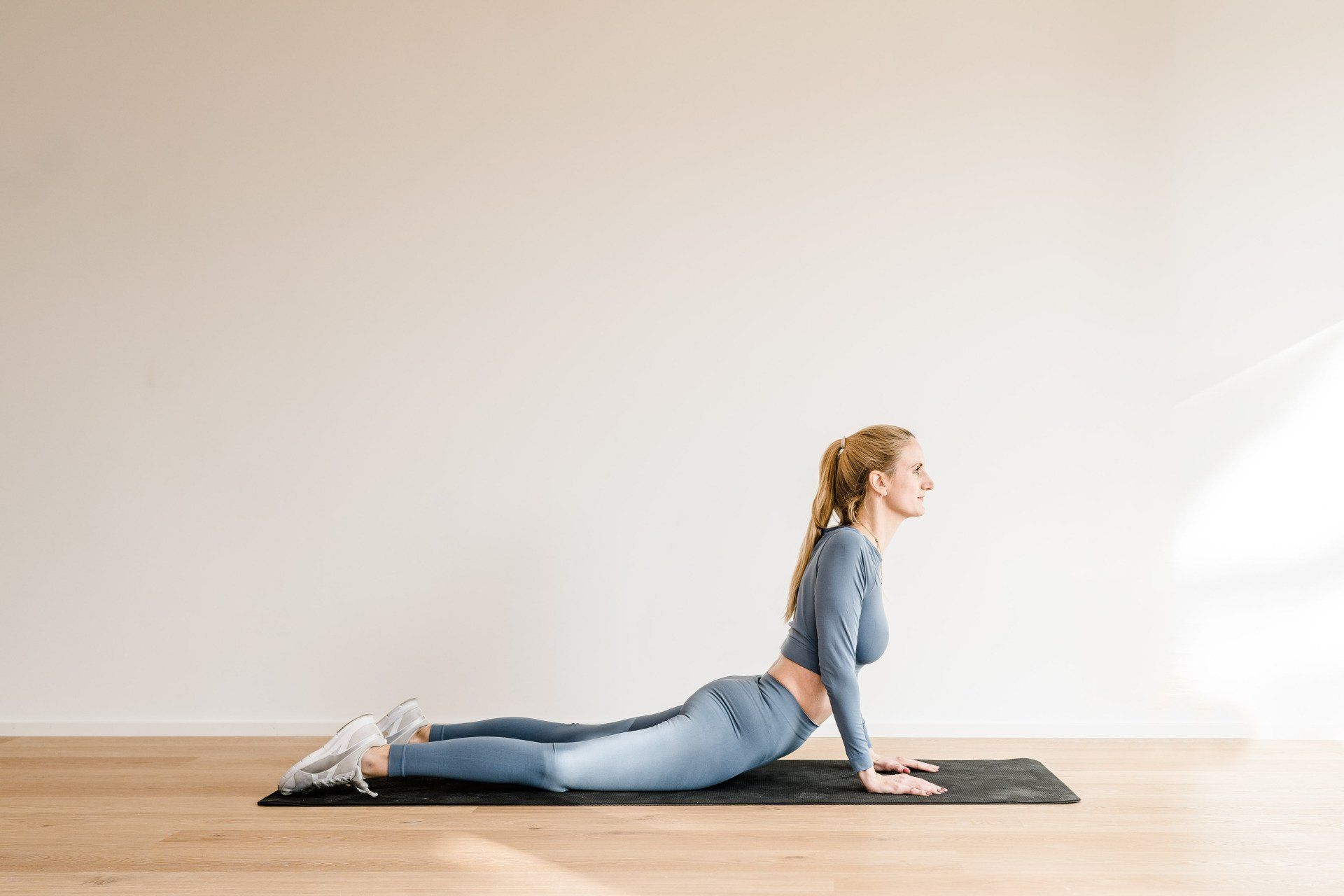 Fit mit Rückbildung - Mein Rückbildungskurs für alle Mamas nach der Geburt Julez beim Yoga. Sie liegt auf dem Bauch auf der Sportmatte und streckt den Oberkörper nach oben. Diese Position heißt Kobra.
