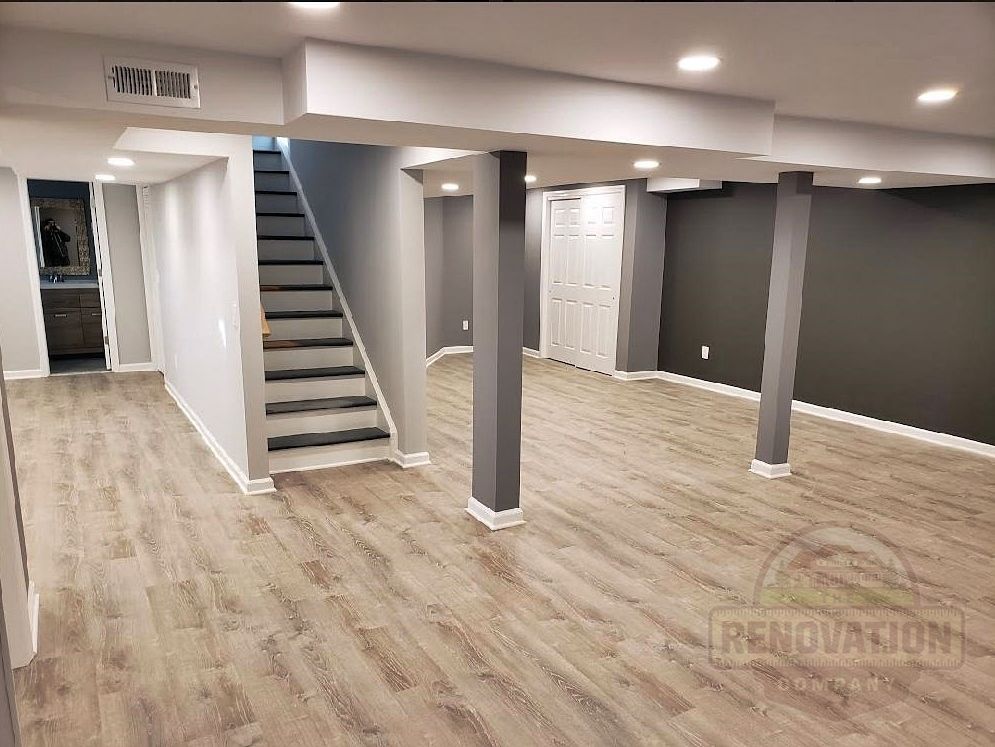 The Renovation Company finished basement with LVT flooring, dark gray walls, white trim, and recessed LED lighitng