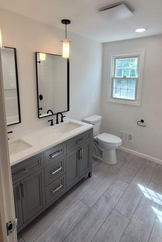 Remodeled bathroom by The Renovation Company with a double-basin vanity, gray floor tile, pendant lights.