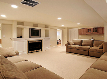 a beautiful basement with a fireplace, TV, and light brown sofas