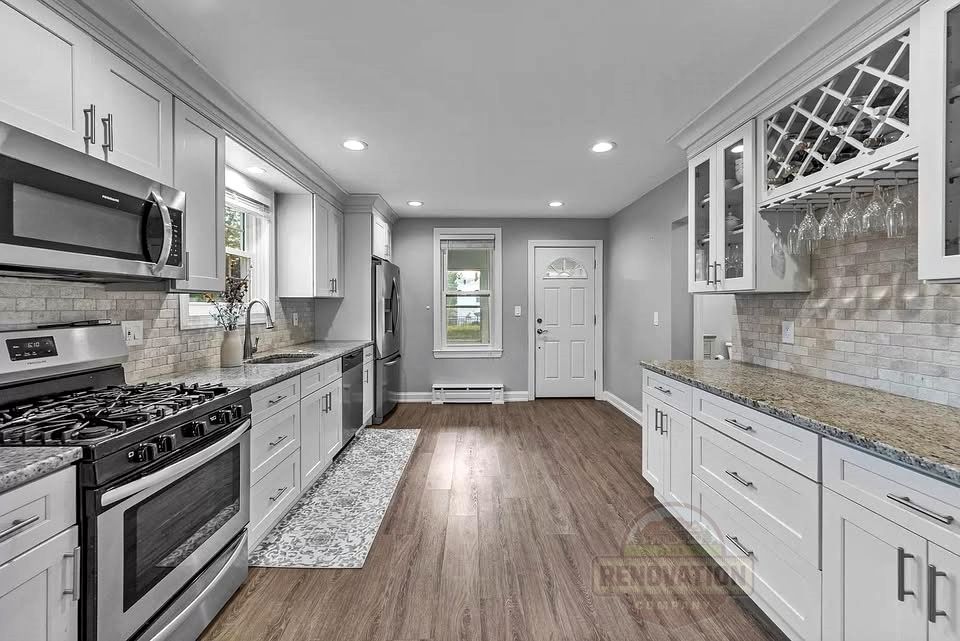 Remodeled kitchen by The Renovation Company with white cabinets, granite counters, and new stainless steel appliances.