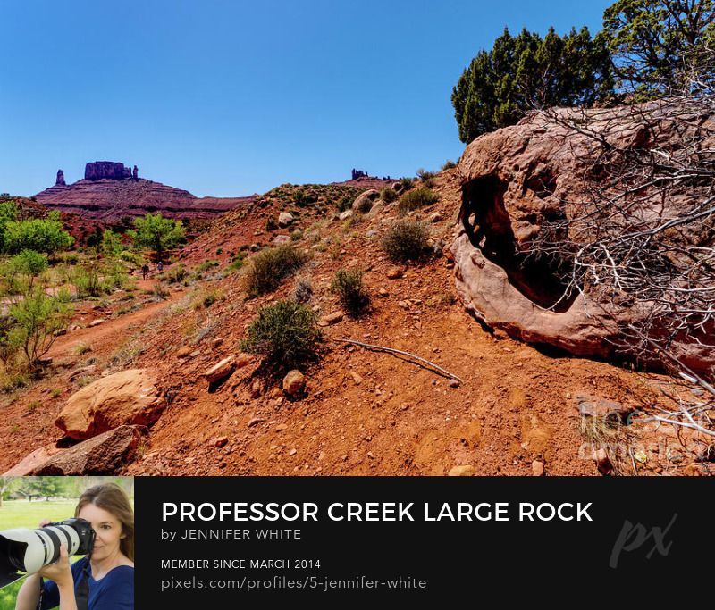 A large rock with a hole in it seen while hiking trail at Professor Creek and Mary Jane Canyon. In the background you can see a mesa rock formation. This is located in the desert in Moab, Utah. Photo by Jennifer White with Timeless Moments Photography.