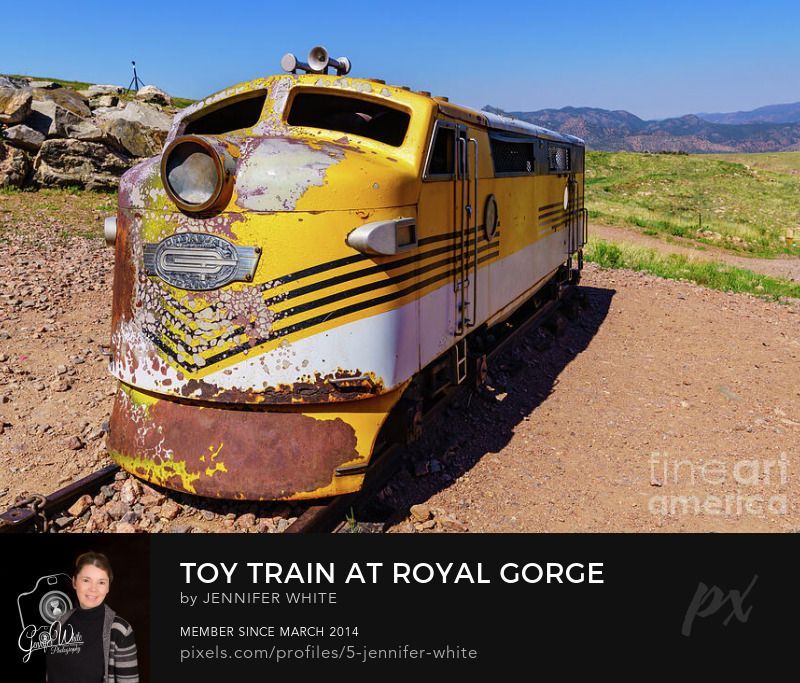 A cute little yellow train toy sits on a playing area at the Royal Gorge Bridge in Cañon City, Colorado, United States. This locomotive is just large enough for kids to climb into. In the background you can see the wet mountains.