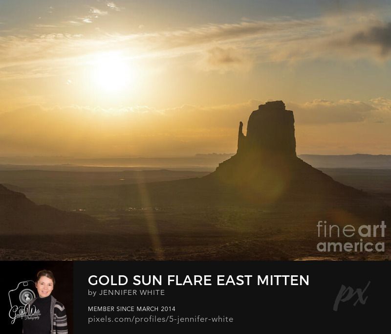Click image to see full photo A golden sun flare during sunrise glows by the East Mitten Butte at Monument Valley in at Navajo Tribal Park in northeast Navajo County, Arizona, United States. There's a morning haze in the air adding a serene atmosphere to this iconic landscape and making the rock formation a silhouette with a sun flare over it. The sun peaks up over some clouds creating some rays. Just beautiful. This is also known as the 7th wonder of Navajoland.