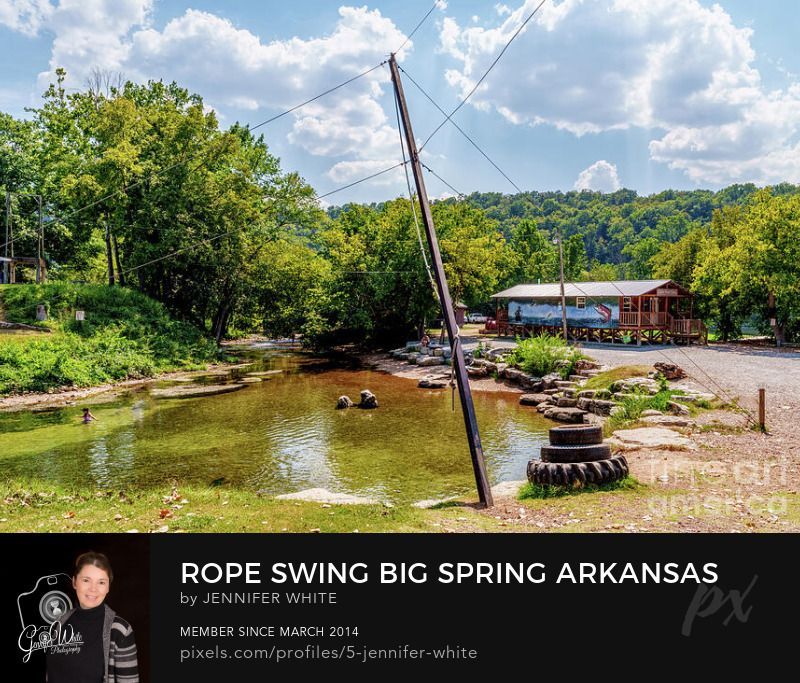 This summer time photograph captures a tall pole that holds a rope swing you can swing on to jump into the natural clear water spring at Big Spring Park in Cotter, Arkansas, United States. The cool natural spring flows thousands of gallons of water up from the ground creating this pool for kids to play in and adults to soak in to get away from the hot summer sun.