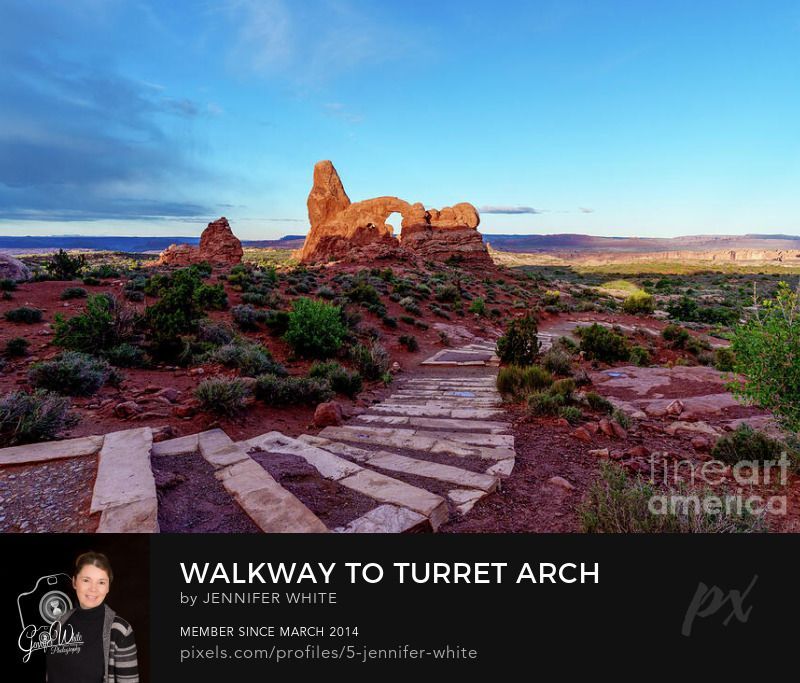 This photograph captures the shadow of the South Window Arch formation as it climbs down the Turret Arch at the Windows Section in Arches National Park in Moab, Utah, USA. It was a quiet desert morning in the iconic park. A curved walkway of stone steps follows the landscape. The bold partly cloudy blue sky contrasts with the sandstone terrain. What a beautiful Southwestern scene giving the eyes an expansive view to enjoy.