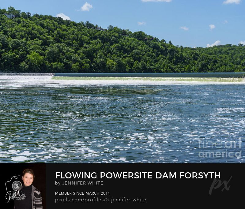 The rushing waters of the White River pour over the historic Powersite Dam in Forsyth, Missouri, United States, creating a dramatic waterfall scene. Built in 1911, this was the first hydroelectric dam in Missouri, forming the Lake Taneycomo reservoir. Also known as the Ozark Beach Dam, the site blends history with natural beauty. In the scene, a few clouds drift across the blue sky, reflecting in the water below, while green trees line the riverbanks for contrast. Power lines stretch across the landscape, a reminder of the dam’s purpose, as bubbles rise and swirl from the powerful force of the cascade. Located just east of Branson, this spot is a unique part of Ozarks history.