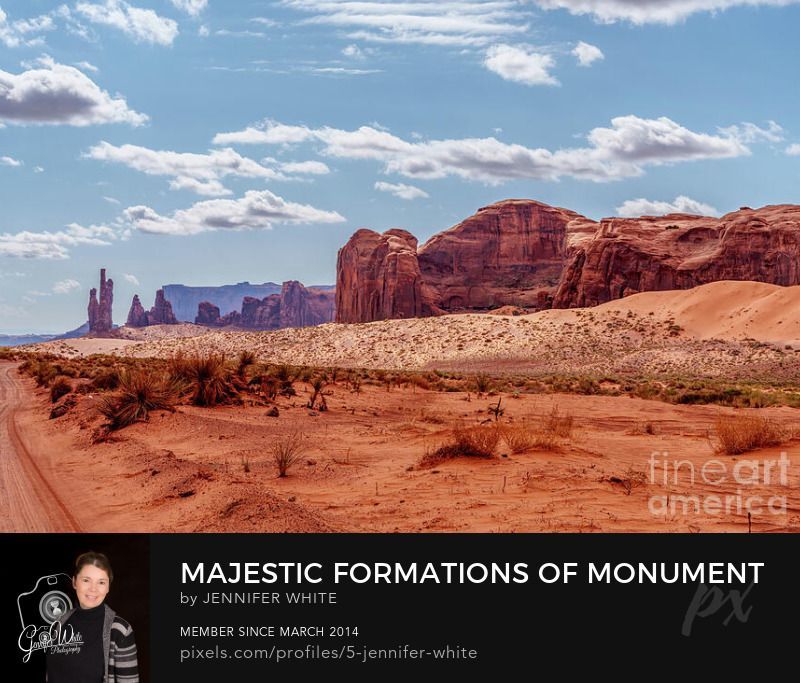 This photograph showcases the breathtaking beauty of Thunderbird Mesa alongside the spires and Totem Pole rock formations in Monument Valley, Arizona, USA. The towering red sandstone formations rise majestically from the desert floor, their rugged shapes and warm hues glowing beneath the soft desert sunlight. A few white clouds drift across the expansive blue sky, adding contrast and balance to the vivid red landscape below. The scene captures the timeless essence of the American Southwest, where wind, sand, and time have sculpted these iconic formations into nature’s masterpieces. This view of Monument Valley’s legendary terrain evokes a sense of peace, wonder, and connection to the enduring spirit of the land.