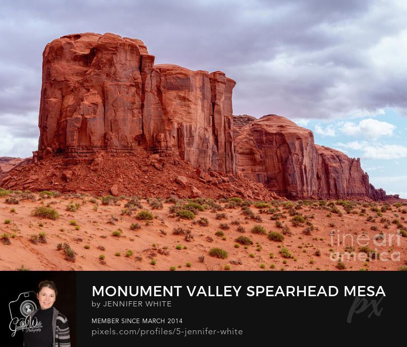 This photo captures one of t angles of the majestic red rock Spearhead Mesa rising from the desert floor in Monument Valley, Arizona, USA, within the Navajo Tribal Park. Storm clouds gather overhead, adding drama and contrast to the vivid desert landscape. With an elevation of 5,998 feet, Spearhead Mesa is named for the sandstone spire above Artist Point that resembles the tip of a spear (not visible in this view). The surrounding Monument Valley desert terrain has scattered sagebrush and desert plants, enhancing the rugged beauty of this iconic Southwest landscape. A true symbol of Navajo Nation’s natural heritage, this scene captures the timeless power and spirit of the American Southwest.