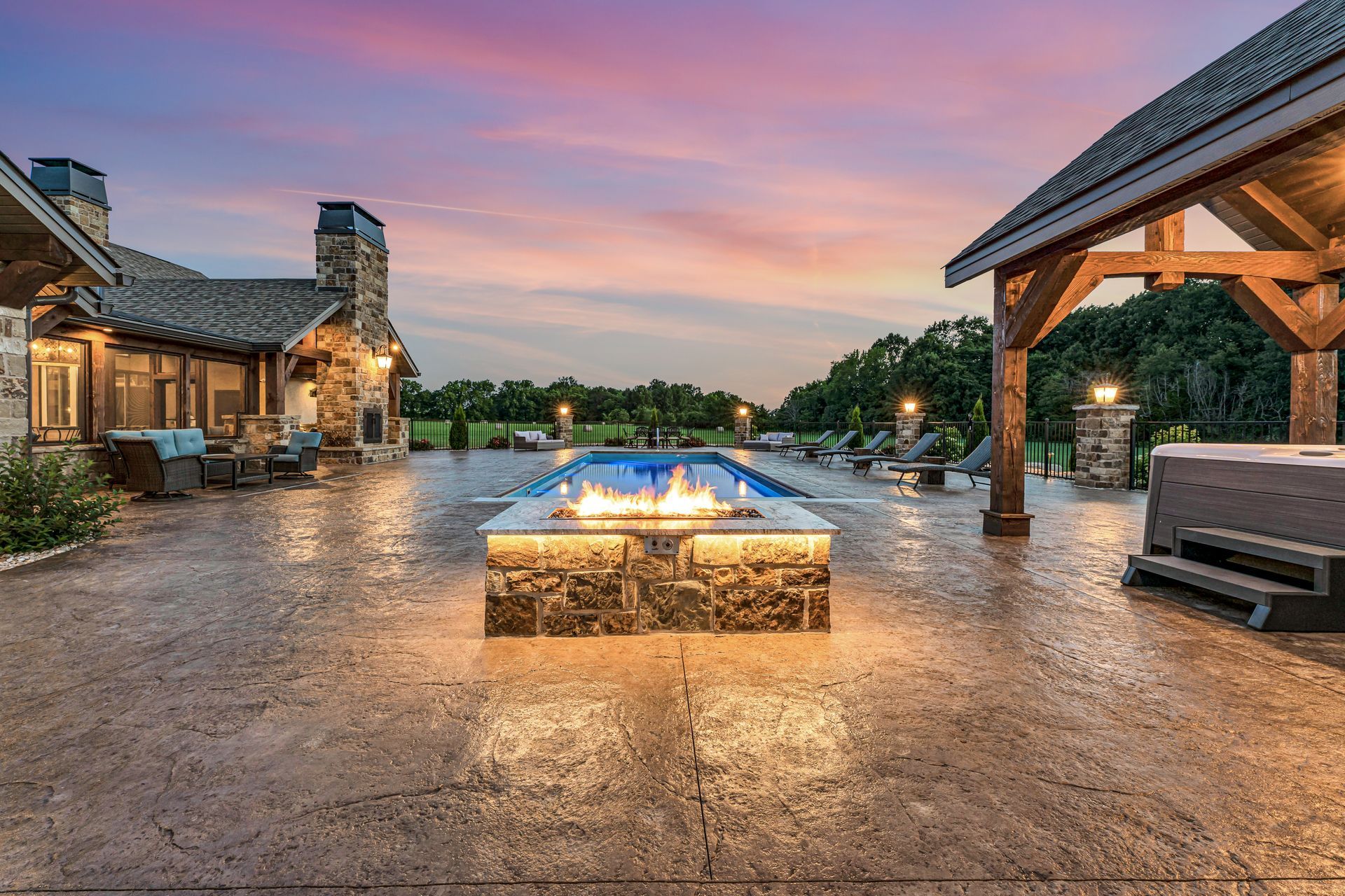 A dusk twilight exterior back patio with pool and firepit of a luxury home in Rogersville, Missouri. Professional photo by Jennifer White Timeless Moments Photography. Home built by Old World Cottages near Springfield Missouri.