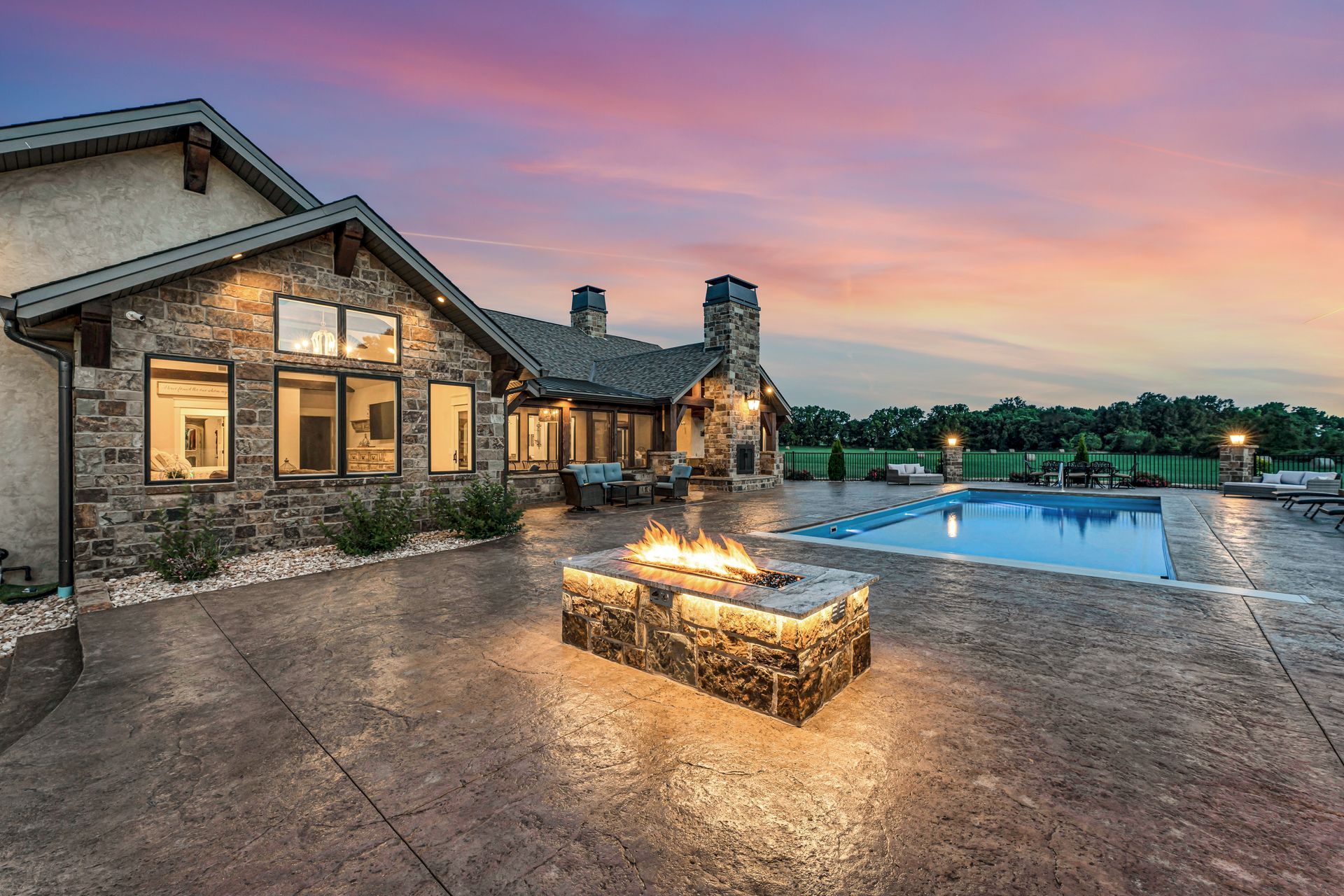 A dusk twilight exterior back patio with pool and firepit of a luxury home in Rogersville, Missouri. Professional photo by Jennifer White Timeless Moments Photography. Home built by Old World Cottages near Springfield Missouri.