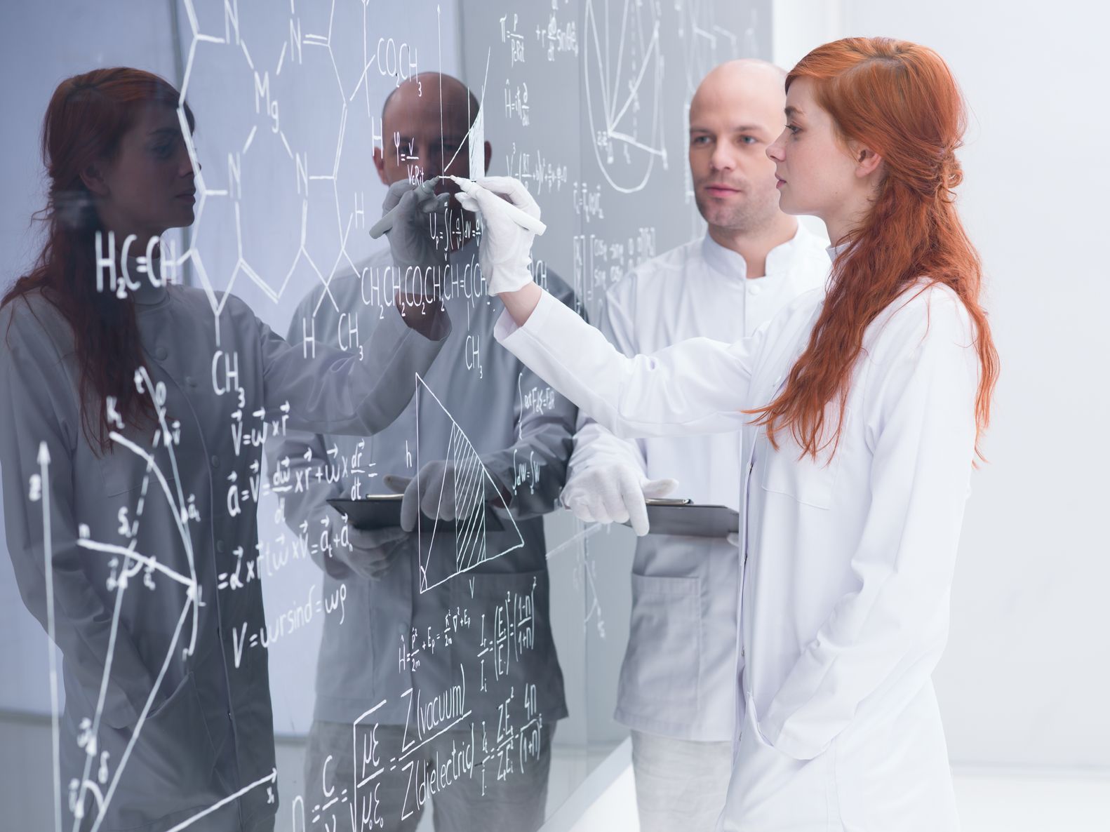 Dozentin und Student stehen gemeinsam an einer Tafel mit chemischen Formeln.