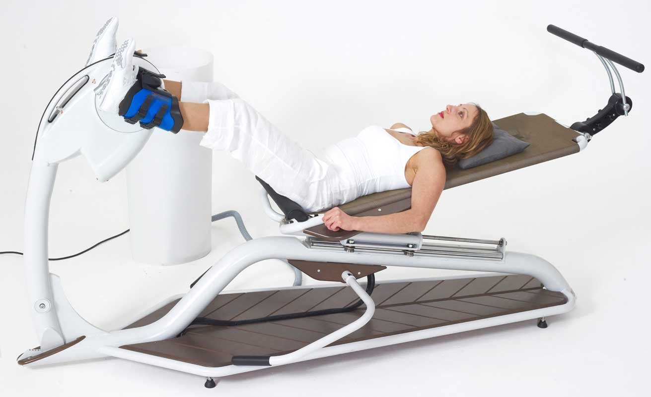 Une dame confortablement allongée sur la couchette, avec les chevilles reliées au pédalier d'Evolis,