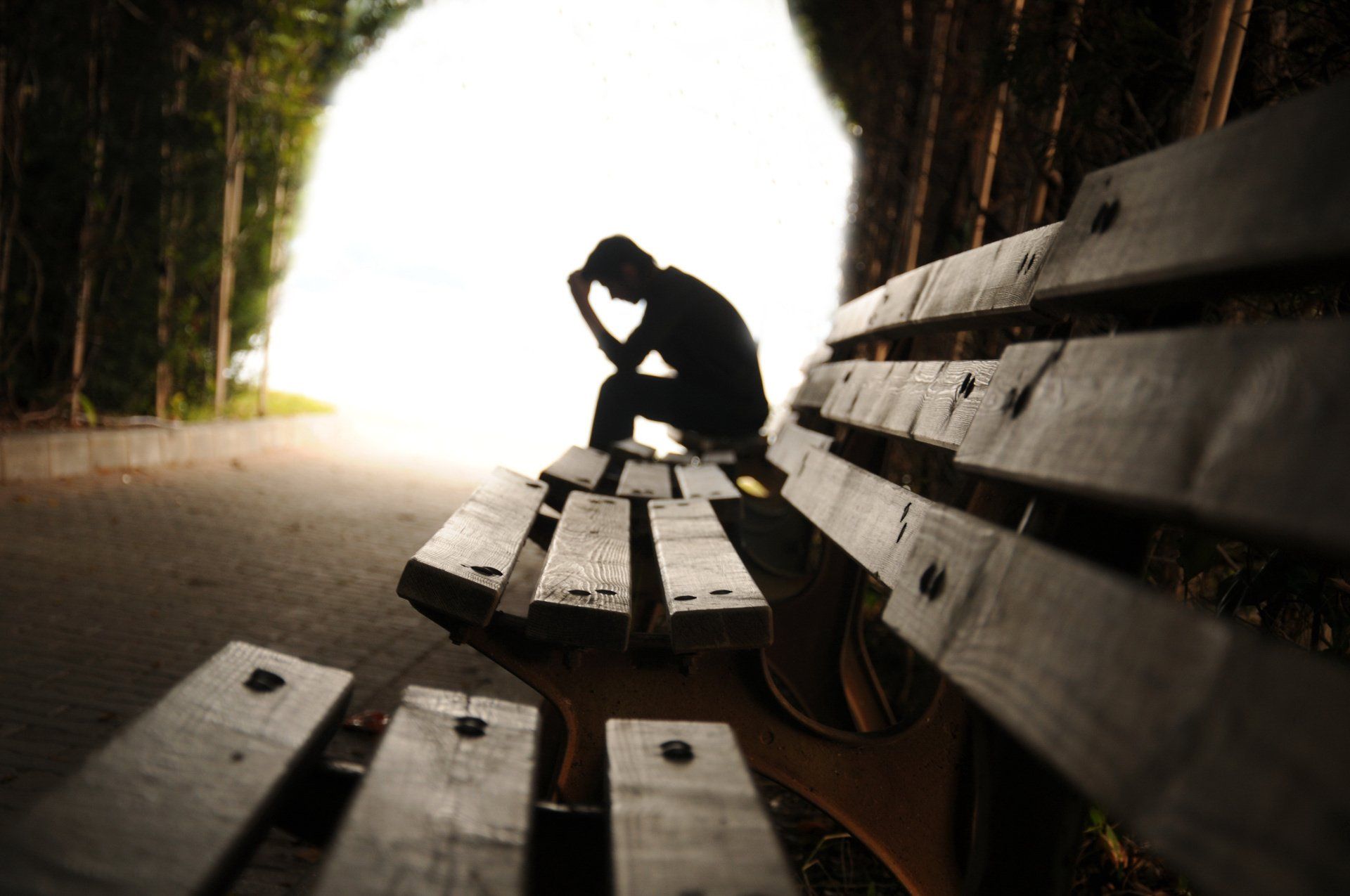 Depressiver Mann sitzt alleine auf einer Holzbank in einem Wald