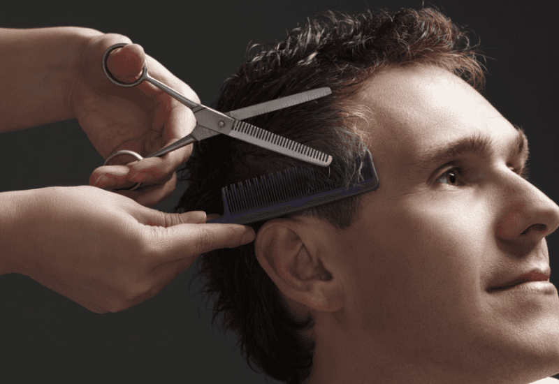 Hands with scissors and a comb giving a man a haircut
