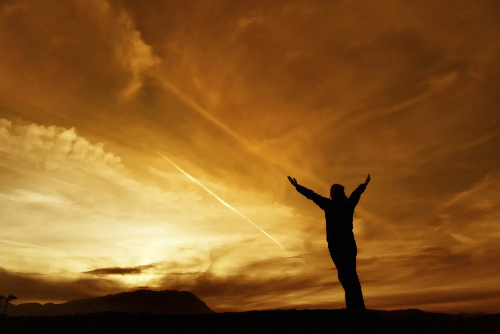 Person in silouette reaching towards golden sky
