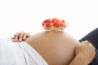 Pregnant lady balancing bowl of fruit on stomach