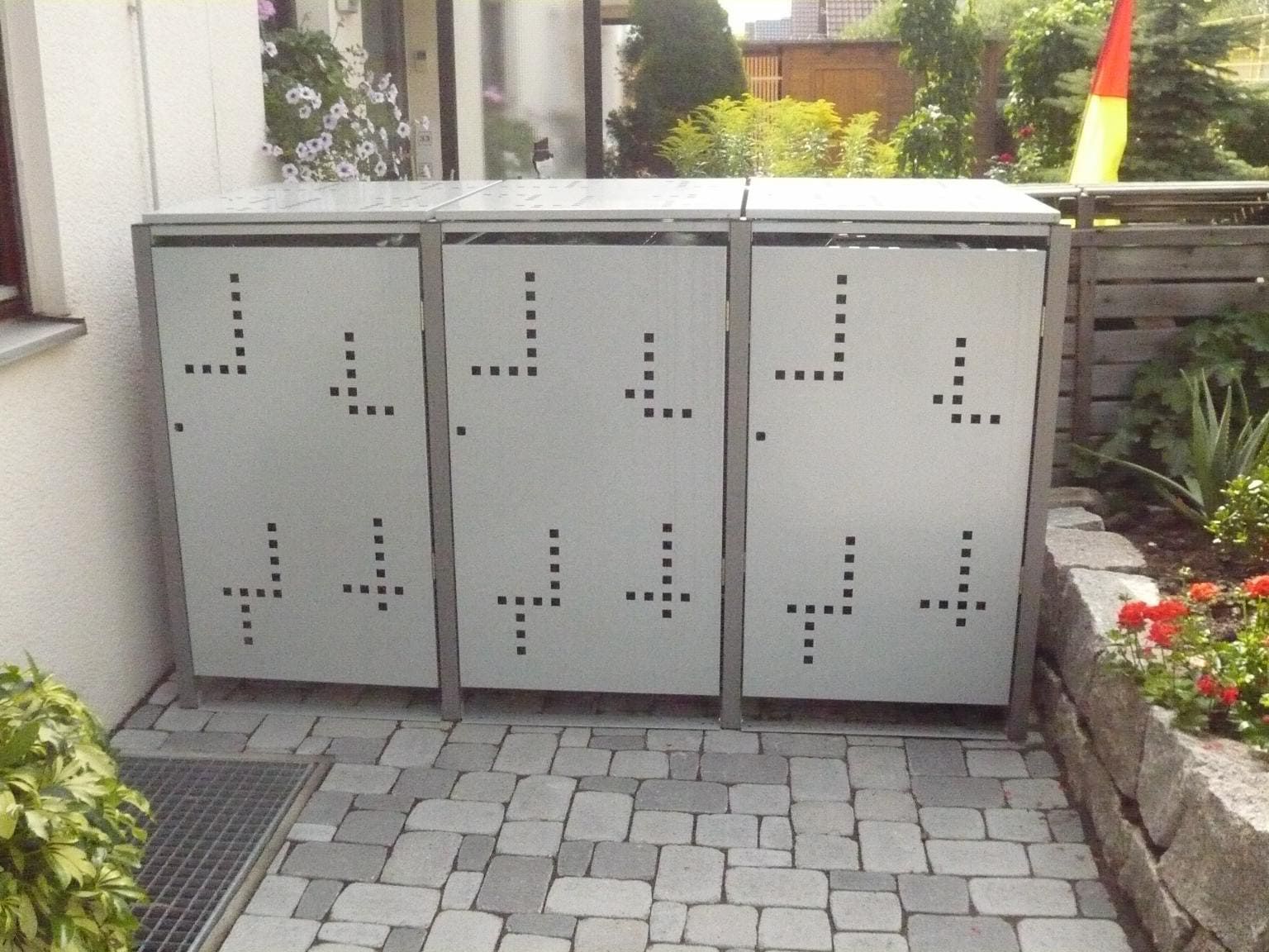 3er Mülltonnenbox aus Metall in hellgrau und dunkelgrau vor einem Haus
