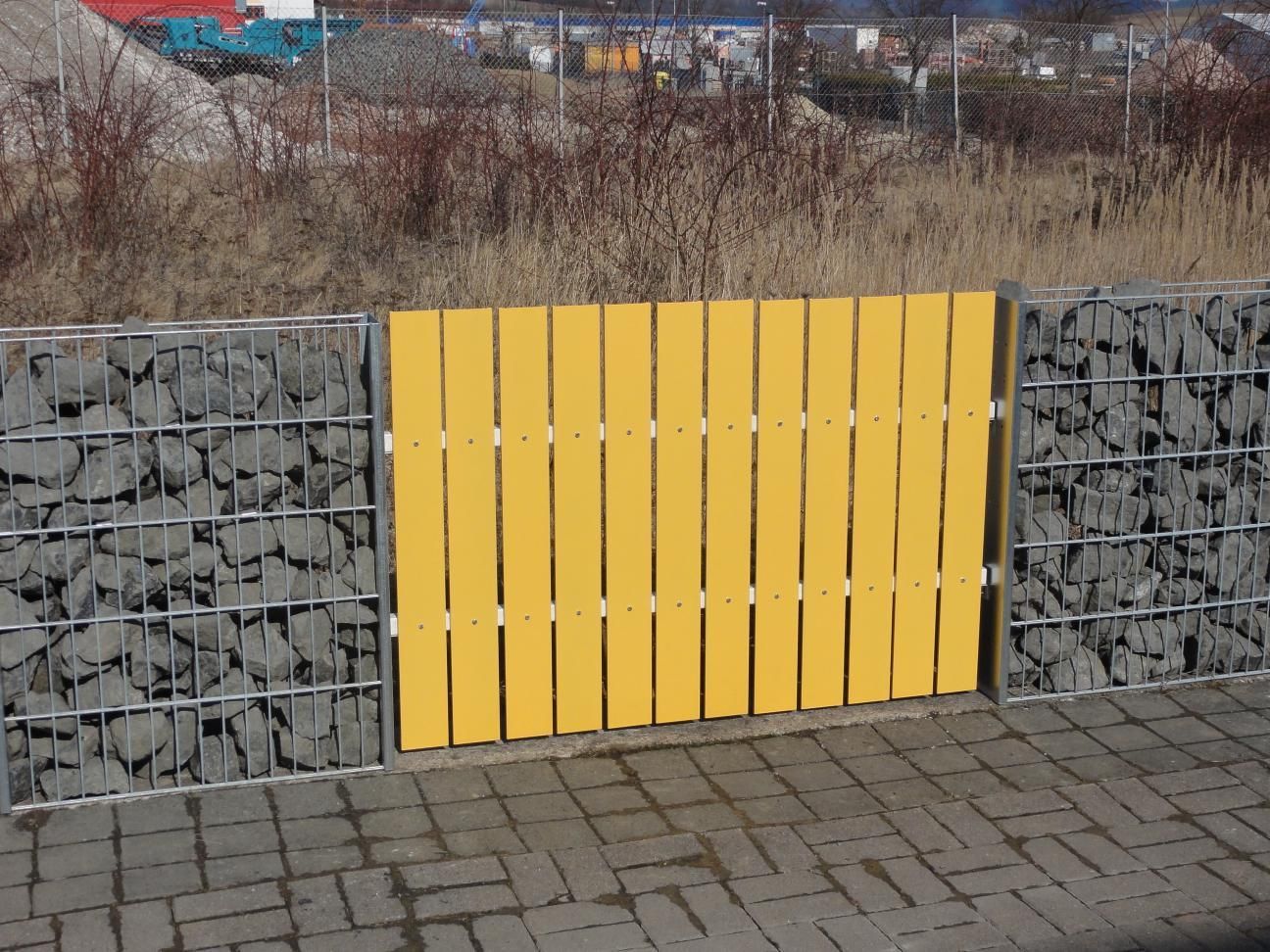 gelber Metall Zaun zwischen zwei Gabionen als modulares Zaunsystem