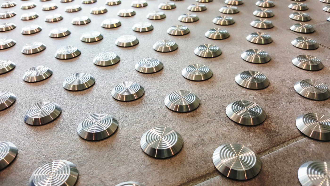 Silberne Noppen eines Bodenleitsystems aus Edelstahl auf Steinboden