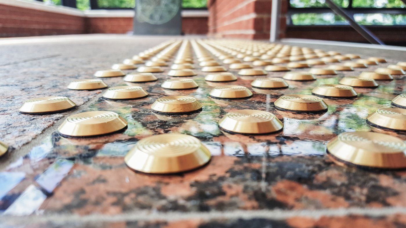 Goldene Noppen eines Bodenleitsystems aus Messing auf marmoriertem Steinboden