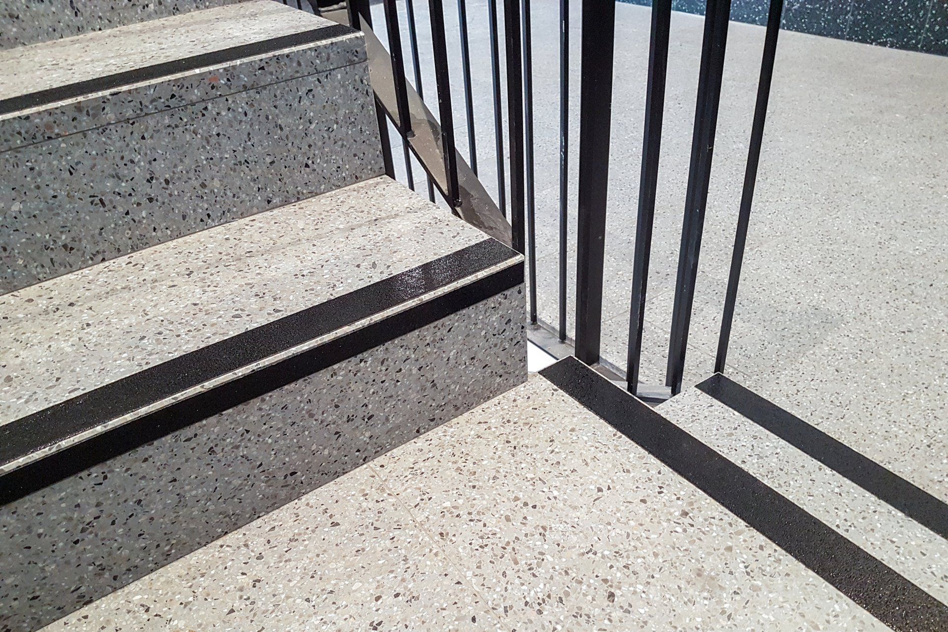 Vier grau gesprenkelte Treppenstufen, mit schwarzen Markierungen.