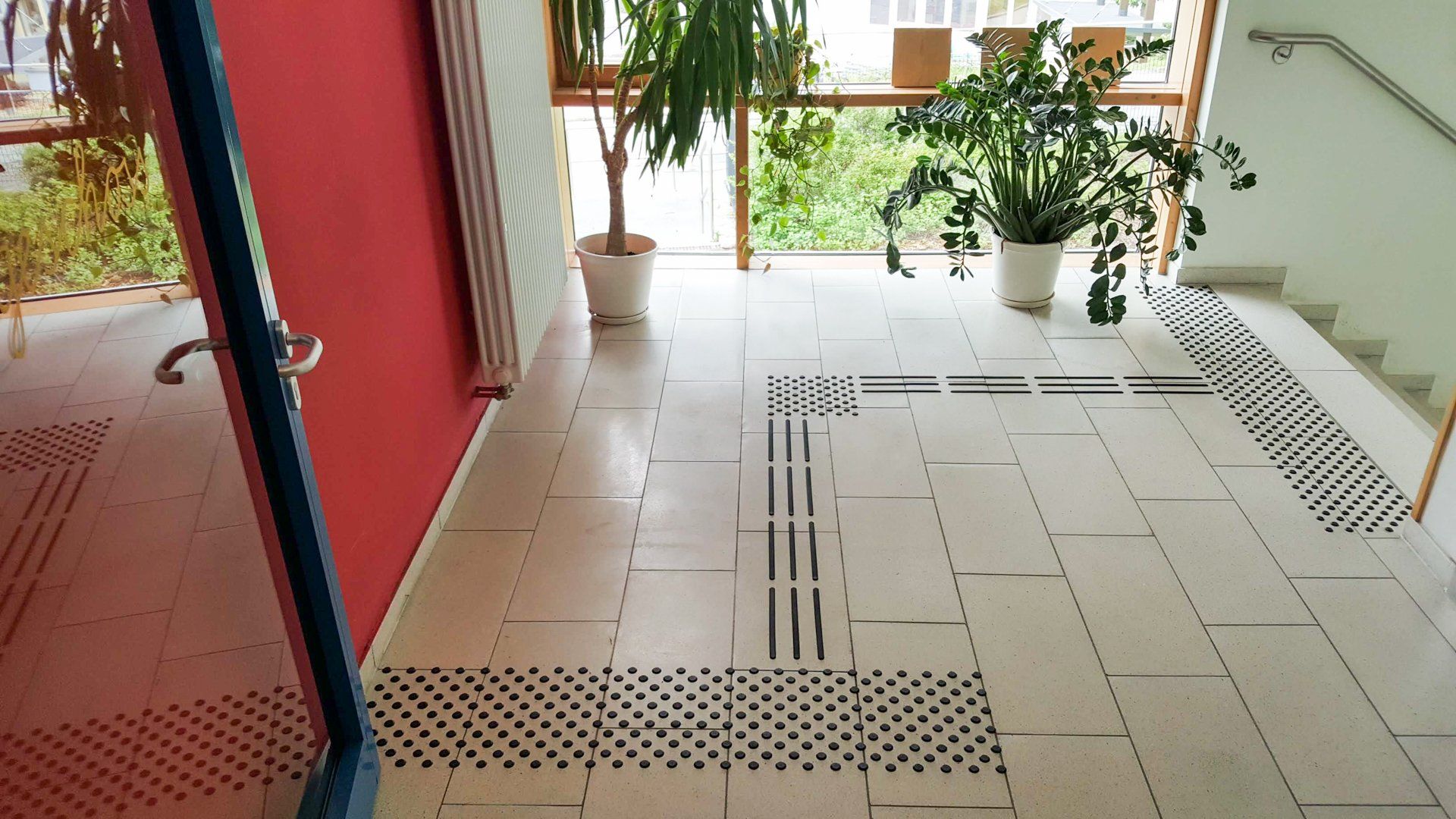 Ein Bodenleitsystem das von einer Treppe zu einer roten Tür führt