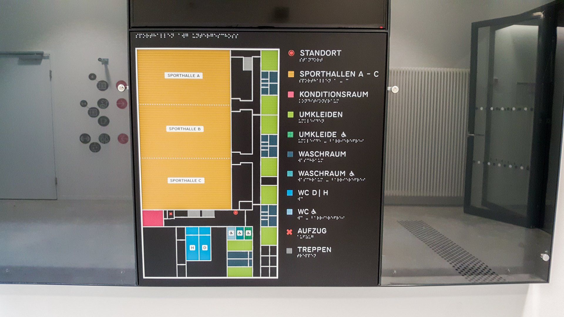 Taktiler Lageplan einer Sporthalle. Es sind drei Hallen, Umkleiden, WCs, Aufzüge und Treppen eingezeichnet
