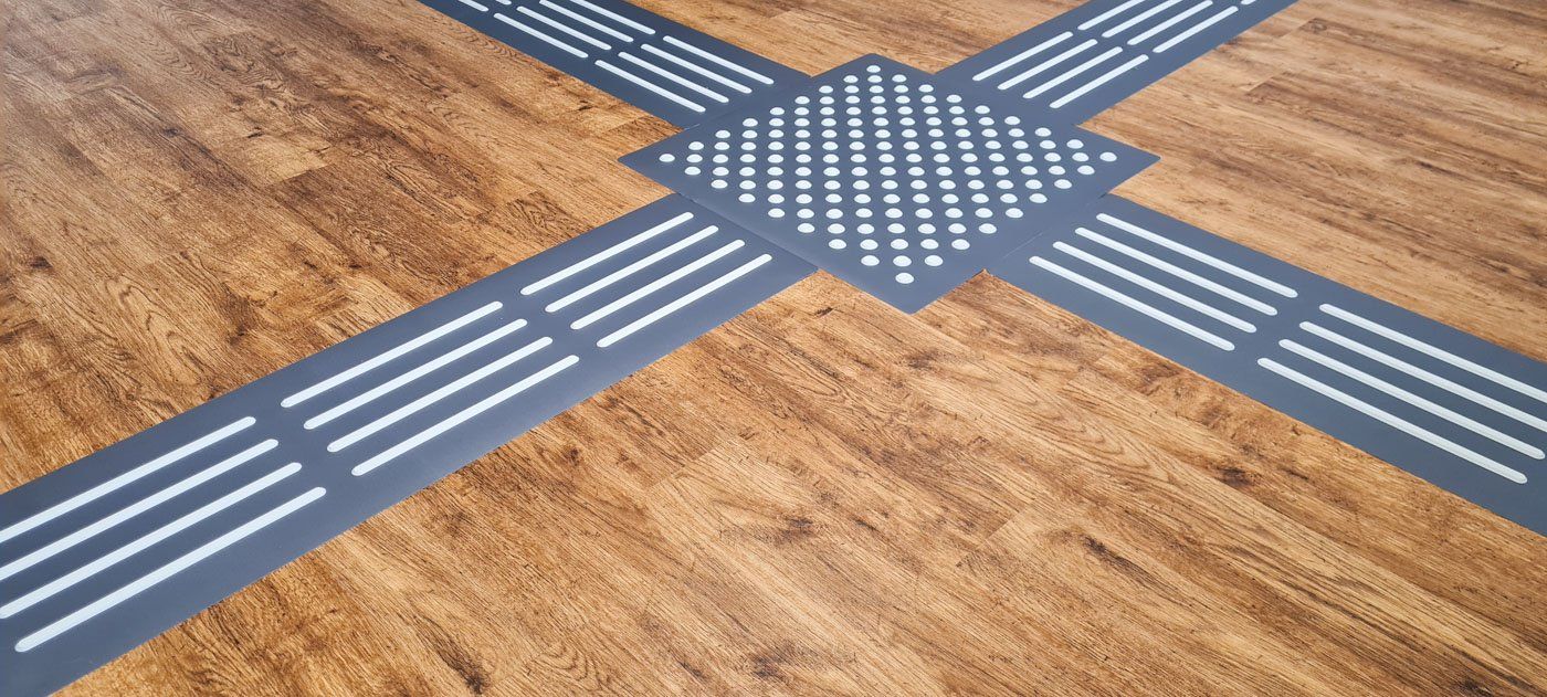 Das TAKTILo Leitsystem auf Laminat verlegt, so dass die Leitlinienfelder und das Noppenfeld eine Kreuzung bilden, die Blinden und seheingeschränkten Menschen hilft, sich zu orientieren.