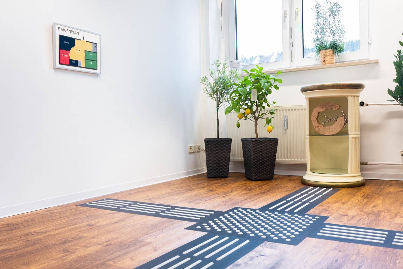 Rippenplatten und ein Aufmerksamkeitsfeld sind auf einem Boden verlegt. Das Aufmerksamkeitsfeld leitet in vier Richtungen weiter. Man kann so zu einem Etagenplan gehen oder einem Beistelltisch kommen.