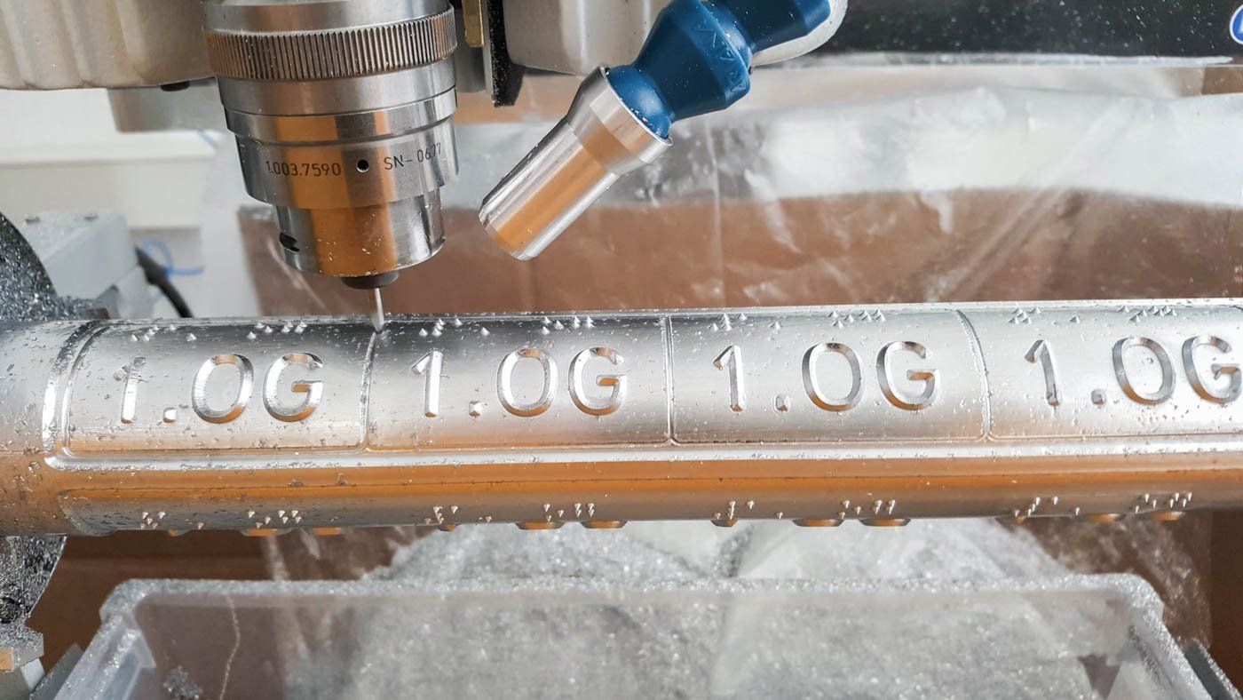 Ein Handlaufschild in der Sonderanfertigung. Eine Maschine schreibt in Blindenschrift 1. OG