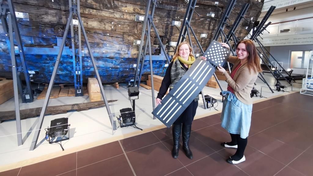 Zwei Frauen halten Bestandteile eines taktilen Bodenleitsystems in den Händen und lächeln in die Kamera.